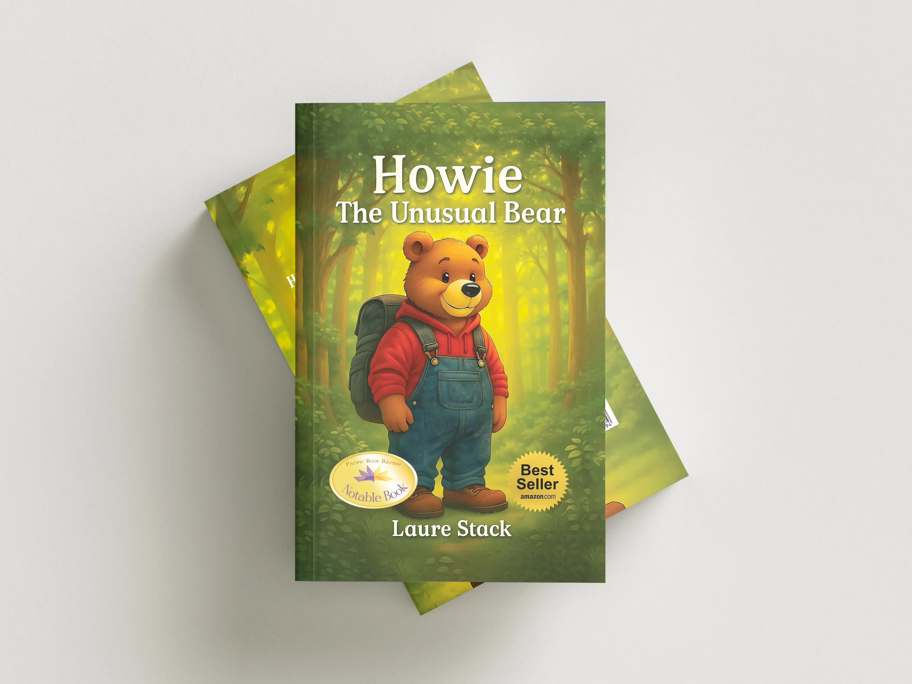 A children's book titled "Howie The Unusual Bear" by Laure Stack, featuring an illustration of a bear in overalls and a backpack on a forest cover, shown standing on top of two matching books against a light gray background.